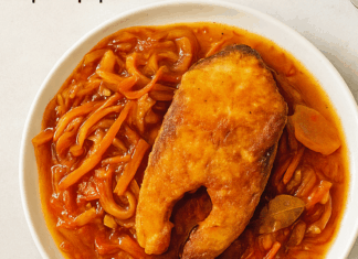 Μερίδες τηγανητού λευκού ψαριού (*) κομμένες και τοποθετημένες μέσα σε βαθύ ταψί, καλυμμένες πλήρως με πλούσια κόκκινη μαρινάδα λαχανικών με καρότα και κρεμμύδια.