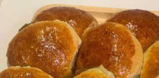 Στρογγυλά χρυσαφί ψωμάκια γεμιστά με καραμελωμένο ζαχαρούχο, αλειμμένα με κρόκο αυγού, σε ταψί με λαδόκολλα.