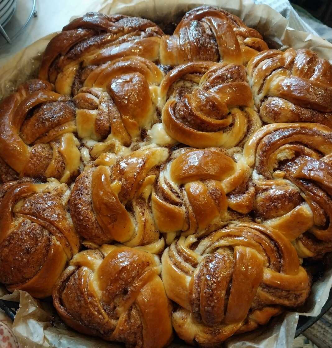 Στρογγυλή φόρμα γεμάτη με ψημένα αφράτα ψωμάκια κανέλας με πλούσια γέμιση, μουλιασμένα σε σιρόπι.