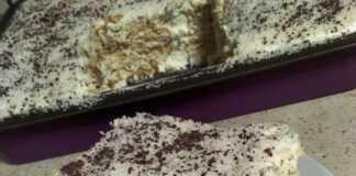 Ένα δροσερό γλυκό ταψιού καλυμμένο με πλούσιο λευκό ινδοκάρυδο και τριμμένη κουβερτούρα, κομμένο σε τετράγωνα κομμάτια