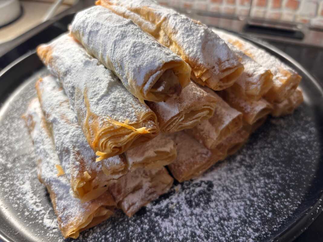 Σειρές από χρυσαφένια τραγανά ρολάκια πασπαλισμένα με πλούσια ζάχαρη άχνη πάνω σε λαδόκολλα.