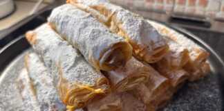 Σειρές από χρυσαφένια τραγανά ρολάκια πασπαλισμένα με πλούσια ζάχαρη άχνη πάνω σε λαδόκολλα.