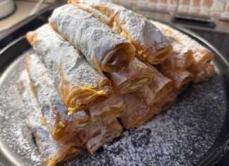 Σειρές από χρυσαφένια τραγανά ρολάκια πασπαλισμένα με πλούσια ζάχαρη άχνη πάνω σε λαδόκολλα.