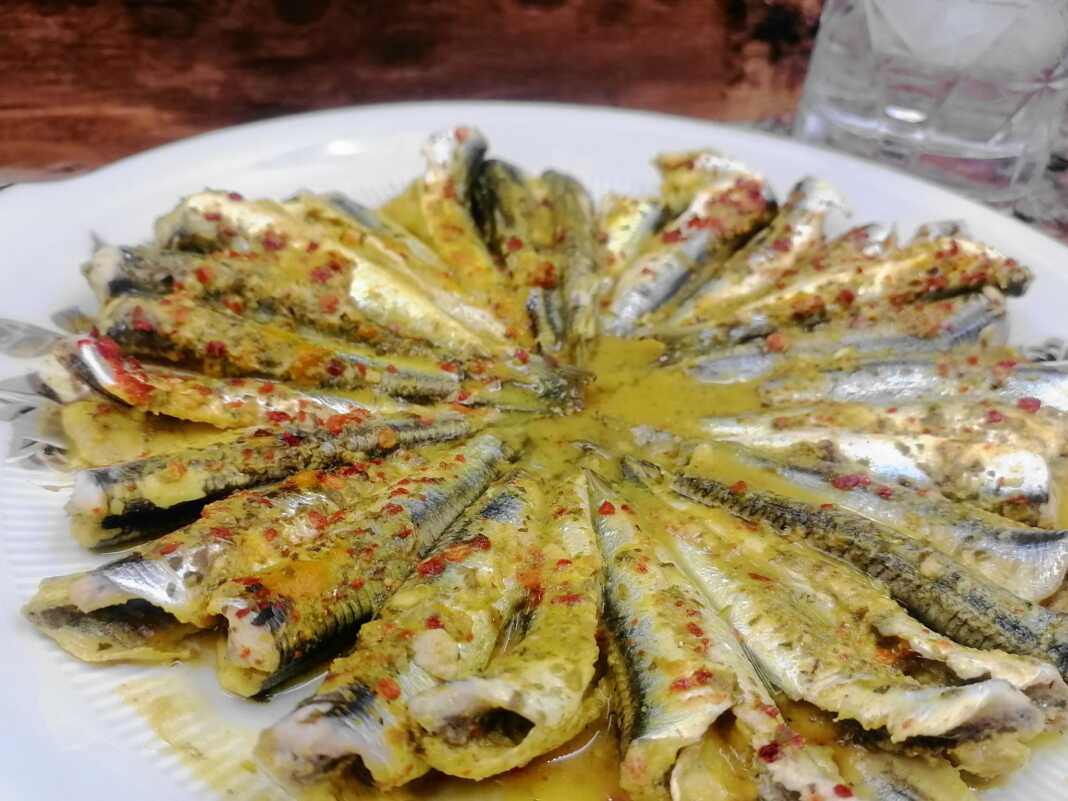 Καθαρισμένες σαρδέλες τοποθετημένες κυκλικά σε πιάτο, μαγειρεμένες με κίτρινη σάλτσα κουρκουμά και κόκκινο μπούκοβο.