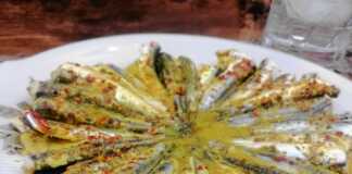 Καθαρισμένες σαρδέλες τοποθετημένες κυκλικά σε πιάτο, μαγειρεμένες με κίτρινη σάλτσα κουρκουμά και κόκκινο μπούκοβο.