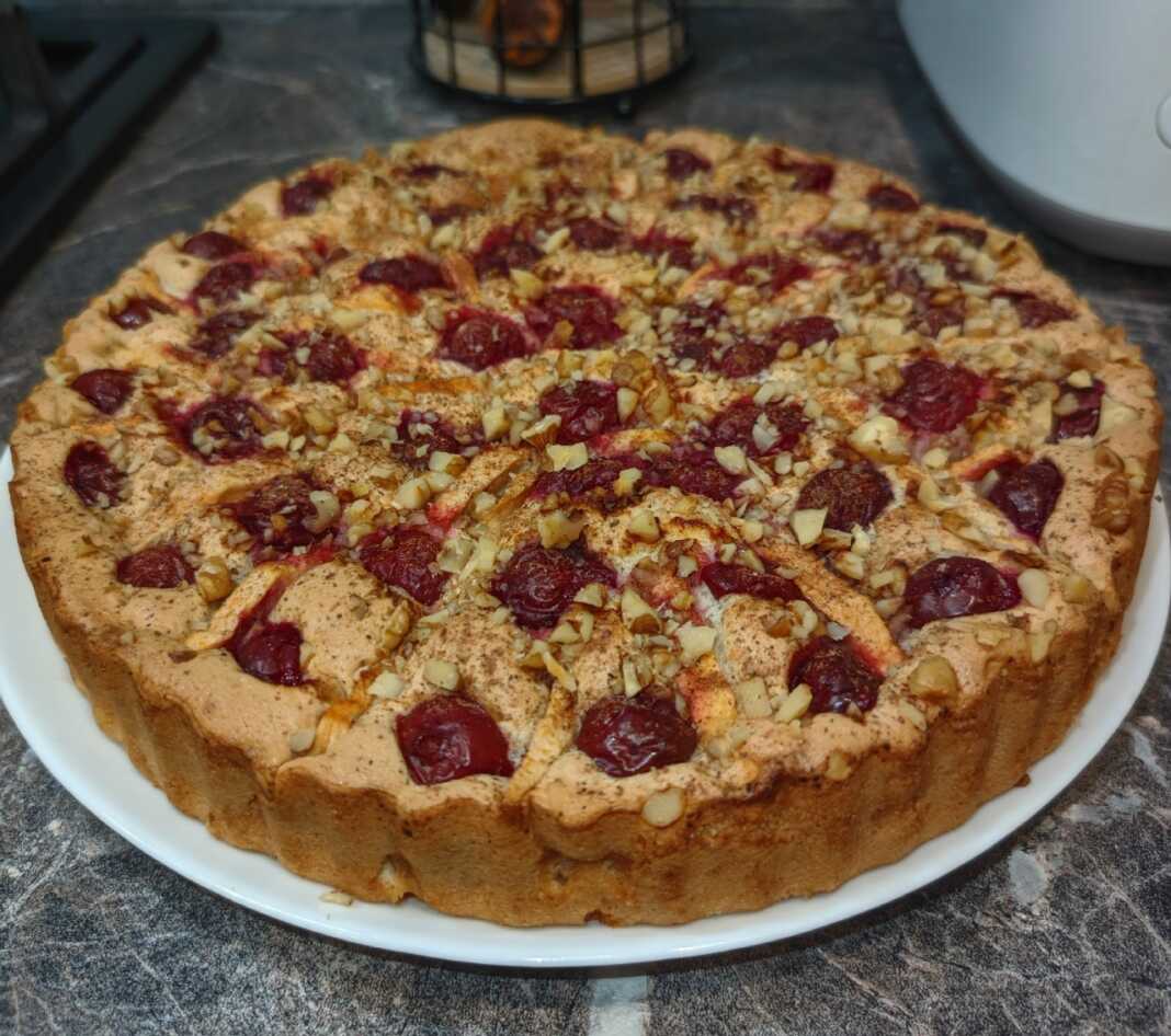 Ένα μεγάλο κομμάτι αφράτου κέικ Σαρλοτ με ροδοκοκκινισμένη κρούστα, γεμιστή με ολόκληρα κεράσια και φέτες μήλου,