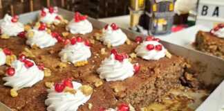 Κομμάτι σιροπιαστής καρυδόπιτας με στρώση σαντιγί, τριμμένο καρύδι και κόκκινους σπόρους ροδιού.