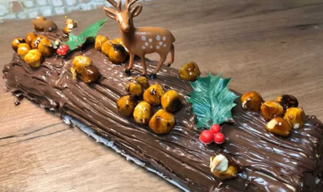 Ένας πλούσιος σοκολατένιος κορμός τυλιγμένος με πραλίνα, διακοσμημένος με ολόκληρα καραμελωμένα φουντούκια και ελαφρώς χαραγμένος για να μιμηθεί τον φλοιό δέντρου.