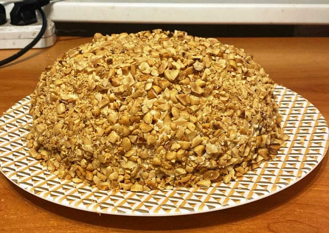 Κομμένη τούρτα με τρία επίπεδα παντεσπάνι και ενδιάμεσα πλούσια κρέμα Σαρλότ, καλυμμένη με κρέμα και ψιλοκομμένα φιστίκια.