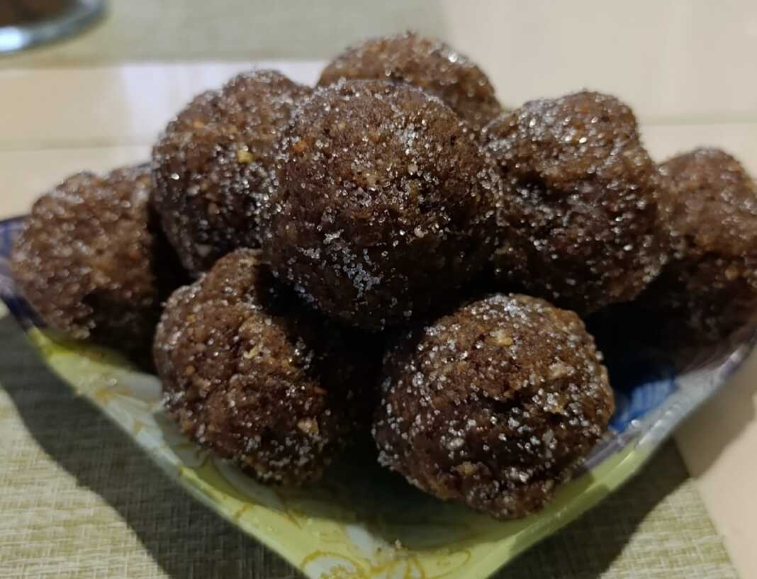 Στρογγυλά σκούρα καφέ τρουφάκια τυλιγμένα σε σκόνη κακάο και ψίχουλα μπισκότου, σερβιρισμένα σε πιατέλα.