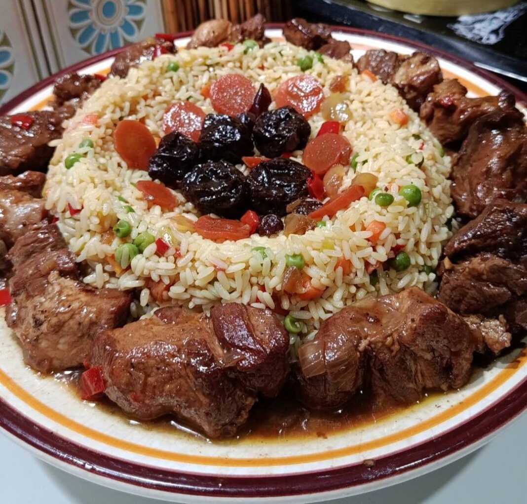 Ζουμερά κομμάτια χοιρινού με μελωμένη σάλτσα δαμάσκηνου, σερβιρισμένα δίπλα σε πολύχρωμο πιλάφι με λαχανικά.