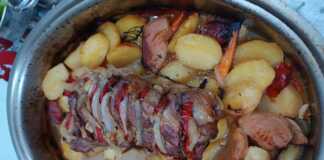 Ένα καλοψημένο χοιρινό ρολό τοποθετημένο πάνω σε μια πανδαισία λαχανικών με πατάτες, καρότα και κυδώνια μέσα σε πήλινη γάστρα.