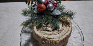 Ένα εντυπωσιακό χριστουγεννιάτικο κέικ κορμός με επικάλυψη σοκολάτας και σχέδια φλοιού δέντρου, στολισμένο γιορτινά.