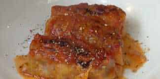 Πίατο γεμάτο με καλοψημένους, κοκκινιστούς λαχανοντολμάδες, περιχυμένους με πλούσια σάλτσα ντομάτας.