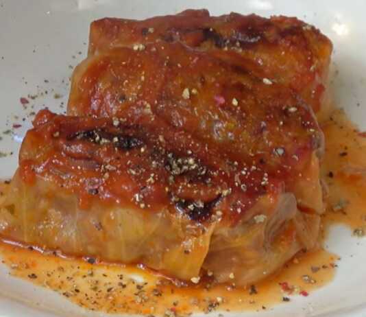 Πίατο γεμάτο με καλοψημένους, κοκκινιστούς λαχανοντολμάδες, περιχυμένους με πλούσια σάλτσα ντομάτας.