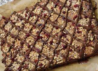 Ένα λαχταριστό κέικ υγείας με επικάλυψη μαύρης σοκολάτας και ξηρούς καρπούς, κομμένο σε φέτες πάνω σε ξύλινη επιφάνεια.