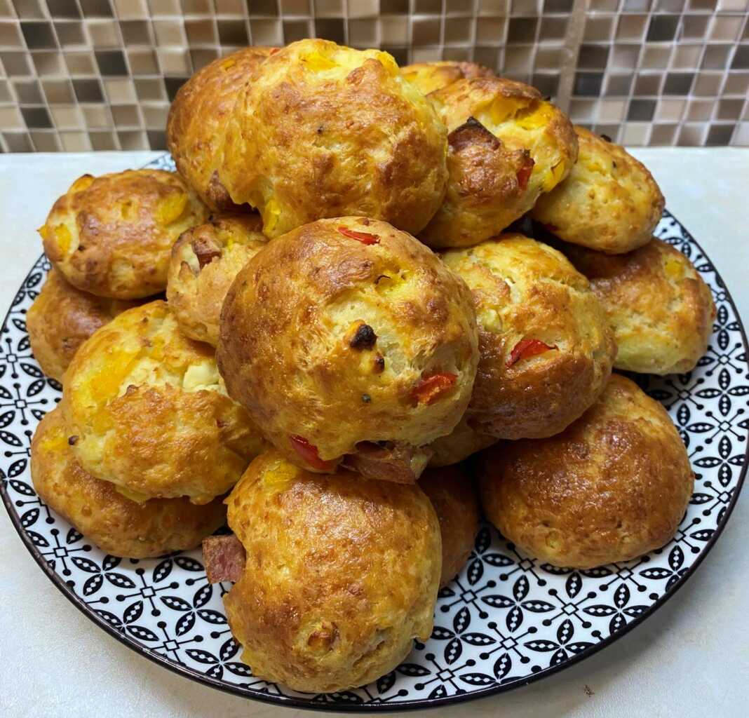 Ένα πιάτο γεμάτο με στρογγυλά ροδοκοκκινισμένα τυροπιτάκια, όπου διακρίνονται κομματάκια από πολύχρωμες πιπεριές στο εσωτερικό τους.