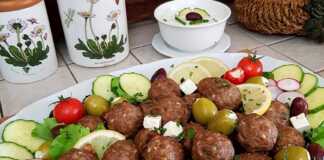 Αρνίσια Κεφτεδάκια στο Φούρνο: Μια Γευστική “Βόμβα” Φρεσκάδας! Μια πιατέλα με καλοψημένα αρνίσια κεφτεδάκια, στολισμένα με φρέσκο μαϊντανό, δίπλα σε ένα μπολ με κρεμώδες τζατζίκι και φέτες λεμονιού.