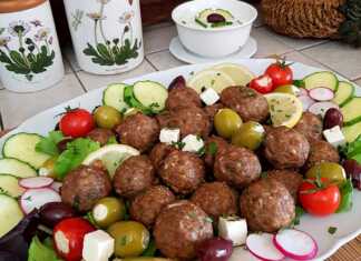 Μια πιατέλα με καλοψημένα αρνίσια κεφτεδάκια, στολισμένα με φρέσκο μαϊντανό, δίπλα σε ένα μπολ με κρεμώδες τζατζίκι και φέτες λεμονιού.