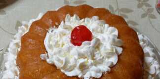 Ένας ζουμερός σιροπιασμένος μπαμπάς σε φόρμα, γαρνιρισμένος με πλούσιες ροζέτες λευκής σαντιγί.