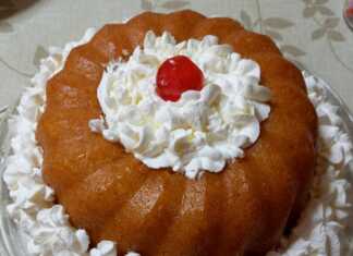 Ένας ζουμερός σιροπιασμένος μπαμπάς σε φόρμα, γαρνιρισμένος με πλούσιες ροζέτες λευκής σαντιγί.