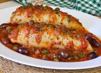 2 μεγάλα γεμιστά καλαμάρια μέσα σε μια πλούσια κόκκινη σάλτσα με ντοματίνια, ελιές και κάπαρη, σερβιρισμένα σε ένα πήλινο σκεύος.