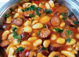 Μια βαθιά κατσαρόλα με μελωμένους γίγαντες σε κόκκινη σάλτσα, με ροδέλες από λουκάνικο και ψιλοκομμένο μαϊντανό στην κορυφή.