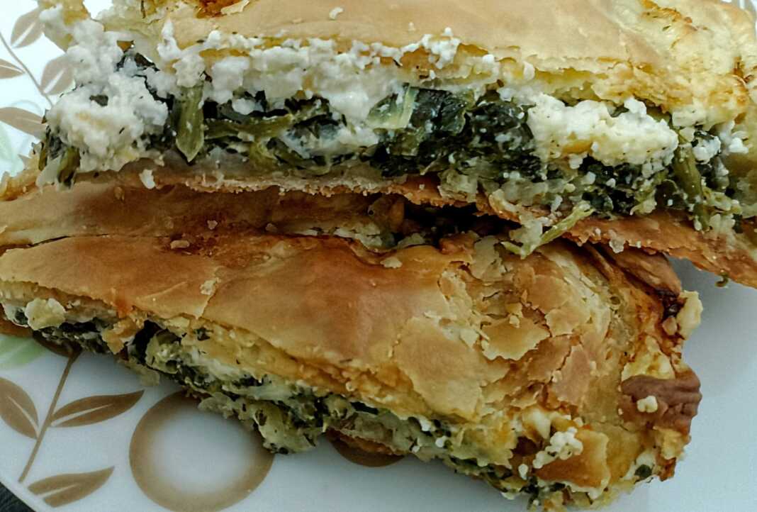 Μια χρυσαφένια και τραγανή σπανακοτυρόπιτα σε κομμάτια που φαίνονται οι στρώσεις των φύλλων και η πλούσια πράσινη γέμιση.