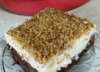 Ένα κομμάτι σιροπιαστής πουτίγκας με βάση καρυδόπιτας και μια παχιά στρώση λευκής κρέμας πατισερί πασπαλισμένο με τριμμένο καρύδι.