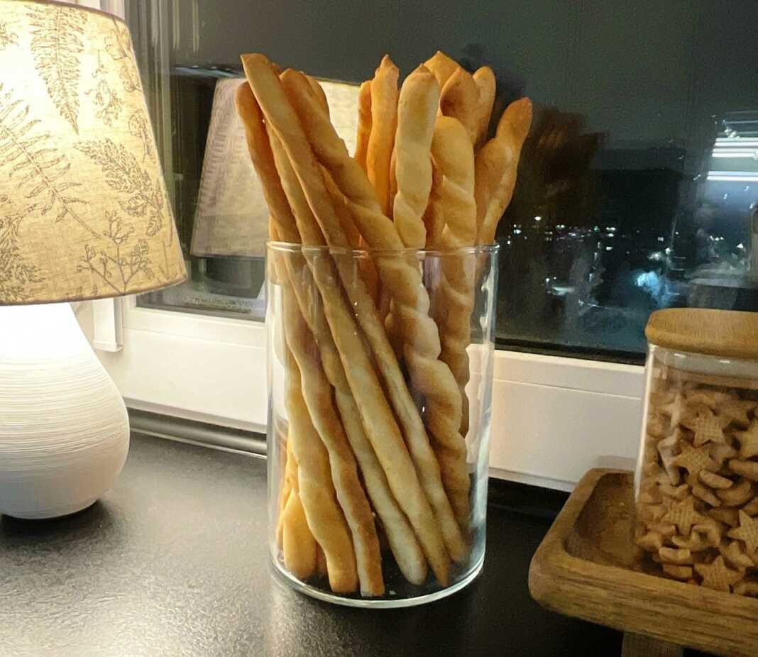 Μια δέσμη από μακριά, χρυσαφένια και στριφτά ιταλικά κριτσίνια μέσα σε ένα γυάλινο βάζο, πασπαλισμένα με σουσάμι.