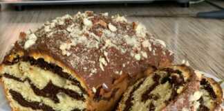 Ένα μακρόστενο μαρμάρινο κέικ με όμορφα νερά σοκολάτας και βανίλιας, καλυμμένο με γυαλιστερό γλάσο σοκολάτας και τριμμένους ξηρούς καρπούς.