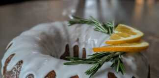 Ένα ολόκληρο σιροπιασμένο κέικ αμυγδάλου πασπαλισμένο με ζάχαρη άχνη, τοποθετημένο σε μια σχάρα, με φέτες πορτοκαλιού δίπλα.