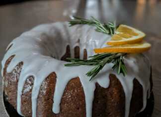 Ένα ολόκληρο σιροπιασμένο κέικ αμυγδάλου πασπαλισμένο με ζάχαρη άχνη, τοποθετημένο σε μια σχάρα, με φέτες πορτοκαλιού δίπλα.