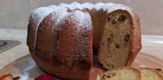 Ένα χρυσαφένιο κέικ γεμάτο σταφίδες, κομμένο σε φέτες πάνω σε μια πιατέλα, έτοιμο για σερβίρισμα.