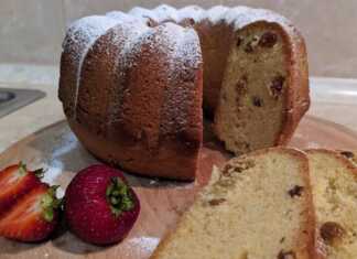 Ένα χρυσαφένιο κέικ γεμάτο σταφίδες, κομμένο σε φέτες πάνω σε μια πιατέλα, έτοιμο για σερβίρισμα.