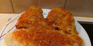 Ένα πιάτο με κομμάτια κοκκινιστού κόκορα σε πλούσια κόκκινη σάλτσα, σερβιρισμένο δίπλα σε ένα λευκό σπυρωτό πιλάφι.