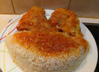 Ένα πιάτο με κομμάτια κοκκινιστού κόκορα σε πλούσια κόκκινη σάλτσα, σερβιρισμένο δίπλα σε ένα λευκό σπυρωτό πιλάφι.