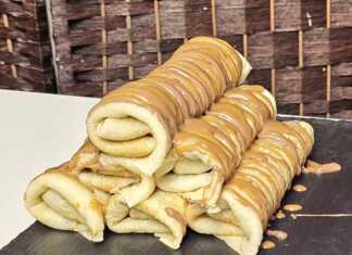 Μια στοίβα από λεπτές, χρυσαφένιες κρέπες σε ένα πιάτο, γαρνιρισμένες με ρευστή πραλίνα φουντουκιού και τριμμένο μπισκότο.