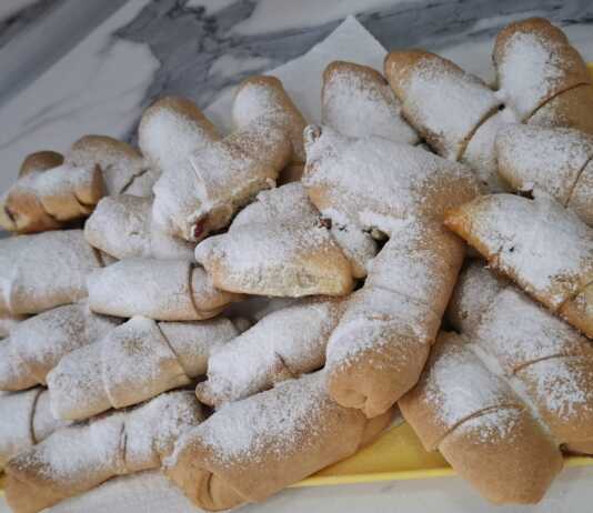 Ένας δίσκος με χρυσαφένια κρουασανάκια πασπαλισμένα με άχνη ζάχαρη, δίπλα σε ένα μπολάκι με μαρμελάδα μήλο.