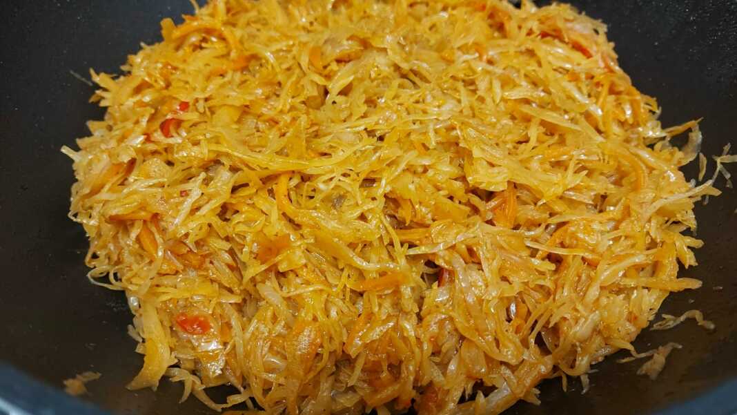 Μια βαθιά κατσαρόλα με αχνιστό λάχανο γιαχνί, κομμάτια κοτόπουλου και πλούσια κόκκινη σάλτσα, γαρνιρισμένη με δάφνη.