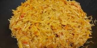 Μια βαθιά κατσαρόλα με αχνιστό λάχανο γιαχνί, κομμάτια κοτόπουλου και πλούσια κόκκινη σάλτσα, γαρνιρισμένη με δάφνη.