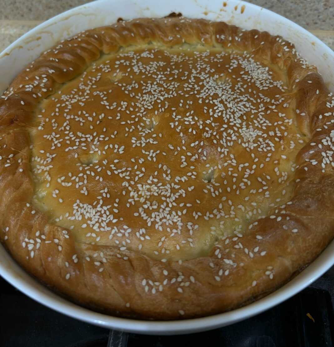 Μια χρυσαφένια, στρογγυλή πίτα με λάχανο πασπαλισμένη με σουσάμι, κομμένη σε τριγωνικά κομμάτια που φαίνονται αφράτα.