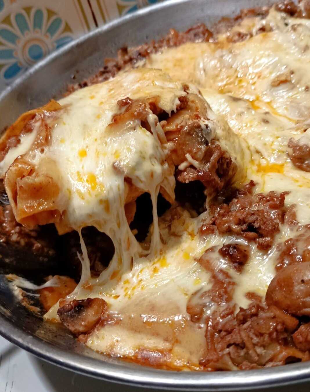 Ένα βαθύ τηγάνι γεμάτο με λαζάνια, πλούσιο κιμά και λιωμένα κίτρινα τυριά που αχνίζουν.