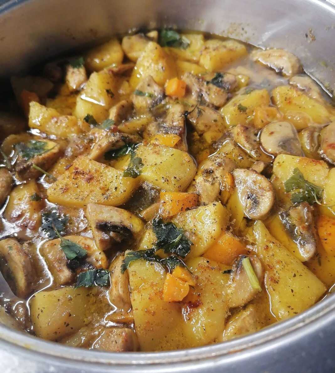 Μια κατσαρόλα με χυλωμένο λεμονάτο φαγητό που περιέχει πατάτες, φέτες από μανιτάρια και ψιλοκομμένο μαϊντανό, σερβιρισμένο σε λευκό πιάτο.