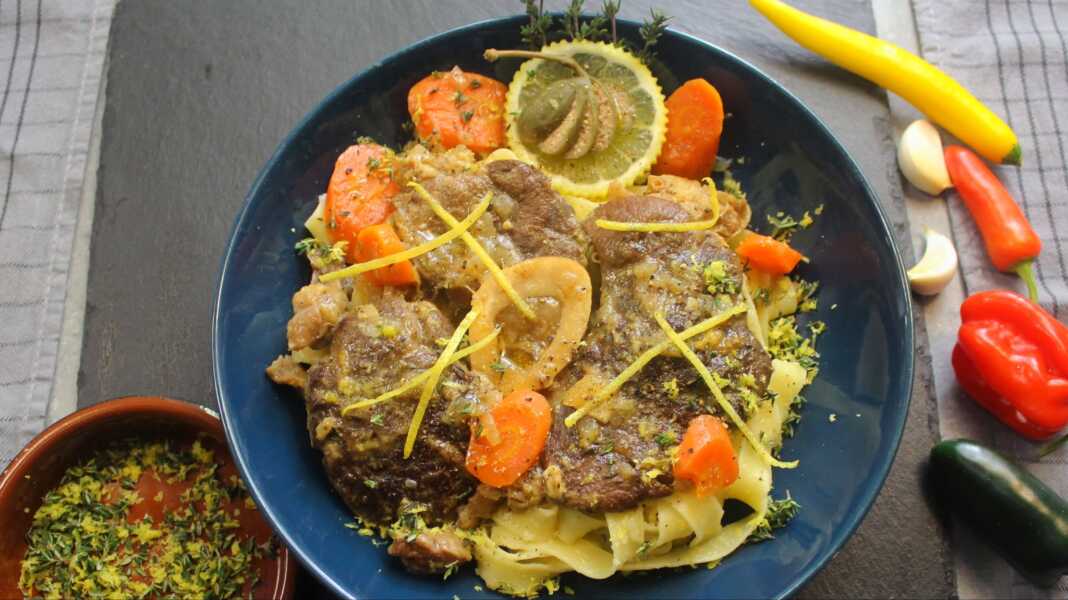 Ένα πιάτο με τρυφερό μοσχαρίσιο οσομπούκο, περιχυμένο με πλούσια λεμονάτη σάλτσα, σερβιρισμένο πάνω σε ζυμαρικά με τριμμένο τυρί.