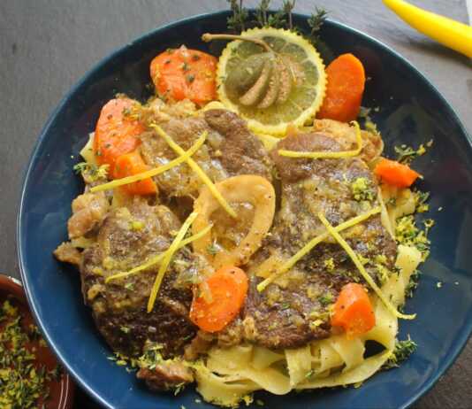 Ένα πιάτο με τρυφερό μοσχαρίσιο οσομπούκο, περιχυμένο με πλούσια λεμονάτη σάλτσα, σερβιρισμένο πάνω σε ζυμαρικά με τριμμένο τυρί.