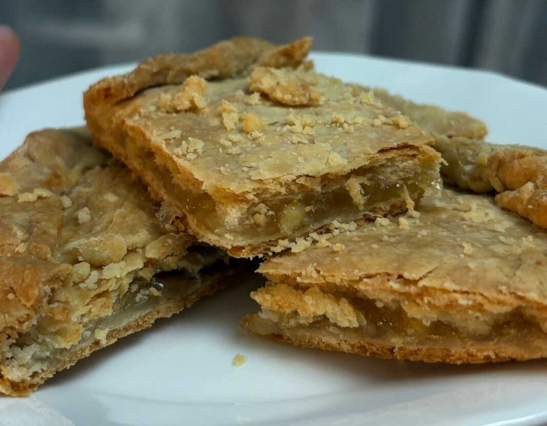 Μια λαχταριστή λεμονόπιτα σε ορθογώνιο ταψί, ροδοκοκκινισμένη και πασπαλισμένη προαιρετικά με άχνη, με την αρωματική γέμιση λεμονιού να φαίνεται στο εσωτερικό της.