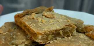 Μια λαχταριστή λεμονόπιτα σε ορθογώνιο ταψί, ροδοκοκκινισμένη και πασπαλισμένη προαιρετικά με άχνη, με την αρωματική γέμιση λεμονιού να φαίνεται στο εσωτερικό της.