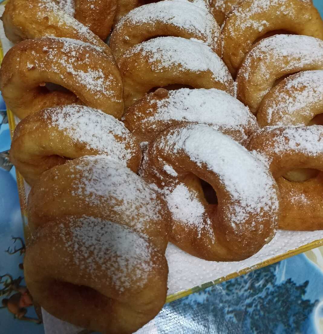 Μικροί χρυσαφένιοι λουκουμάδες με τρύπα στη μέση, πασπαλισμένοι με άχνη ζάχαρη, τοποθετημένοι σε πιατέλα.