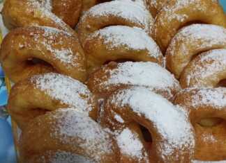 Μικροί χρυσαφένιοι λουκουμάδες με τρύπα στη μέση, πασπαλισμένοι με άχνη ζάχαρη, τοποθετημένοι σε πιατέλα.